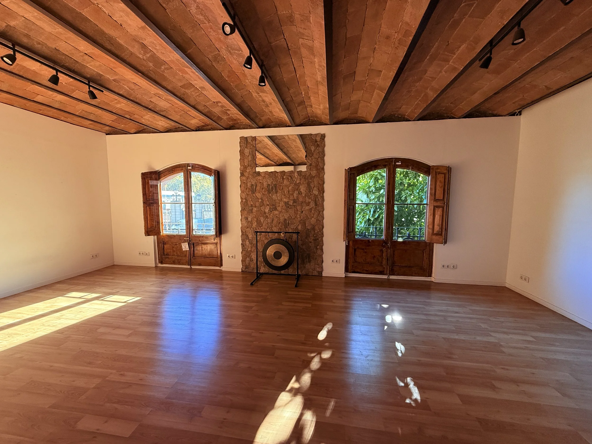 Two arched shuttered windows and a gong in the sunlit Shala