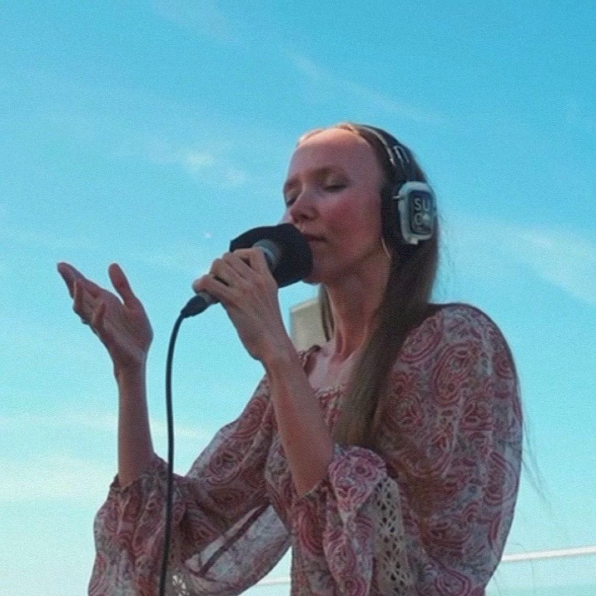 Yulia singing into a microphone under an open sky