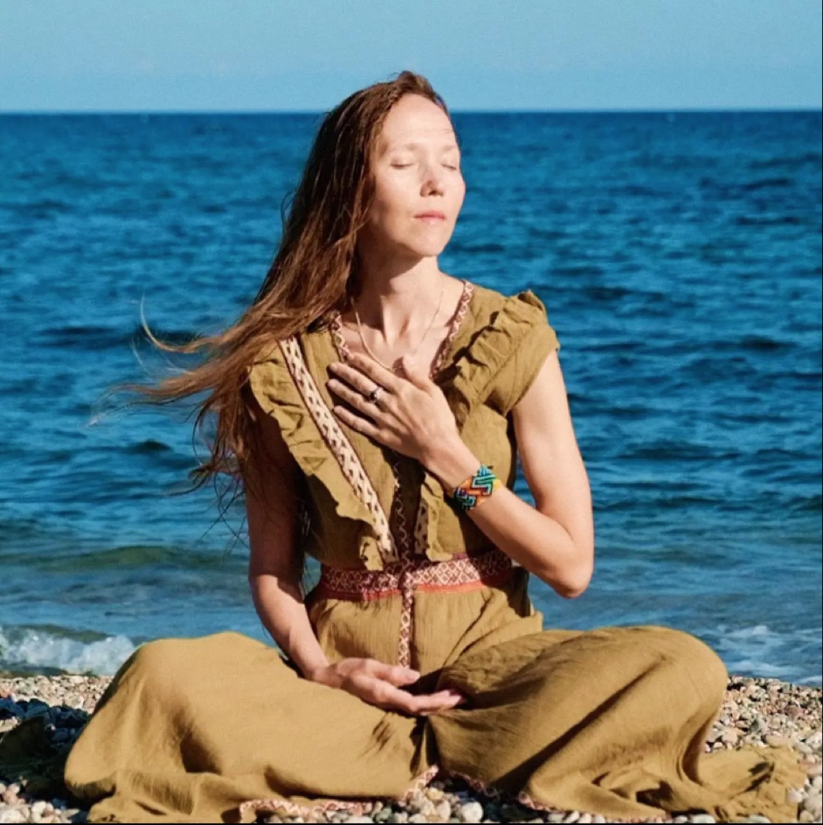 Yulia in seated meditation on a pebble beach by the sea
