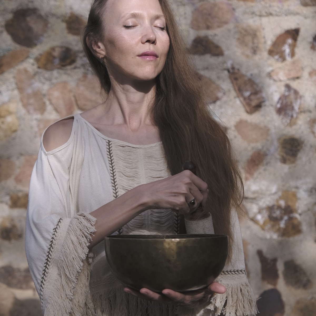 Yulia playing a singing bowl against a stone wall